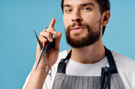 a man hairdresser in a gray apron does his hair on a blue background scissors combの写真素材