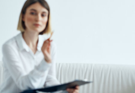 a woman in a shirt with documents in her hands sits on a sofa indoorsの写真素材
