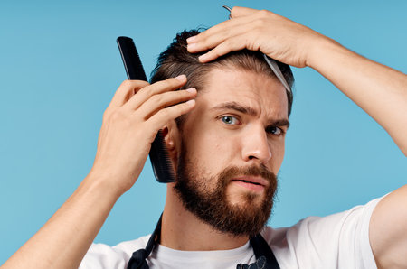 professional hairdresser man in gray apron doing his hair on blue background and cropped viewの写真素材