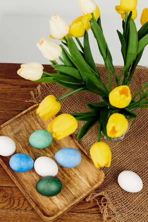 colorful eggs on a wooden tray a bouquet of yellow flowers Easter resurrection of Christ