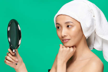 woman of Asian appearance with a towel on her head naked shoulders Looking in the mirrorの写真素材