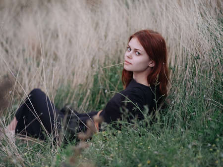 Red-haired Woman in a black dress lies on dry grass in natureの写真素材