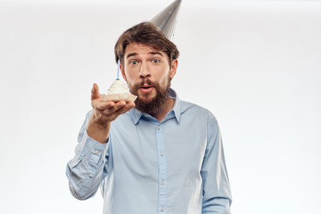 a man with a beard holds a cake in his hand on a light background birthdayの写真素材