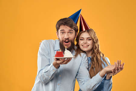Birthday party man and woman on a yellow background in hats with a cake in their handsの写真素材