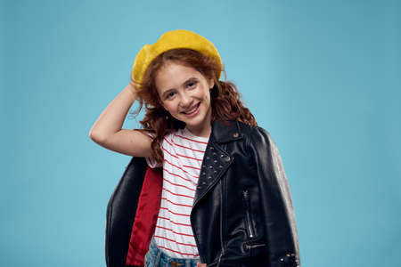 Fashionable girl in a yellow beret and leather jacket striped T-shirt blue backgroundの写真素材