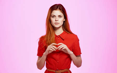 Charming woman in a red dress on a pink background gestures with her hands Copy Space