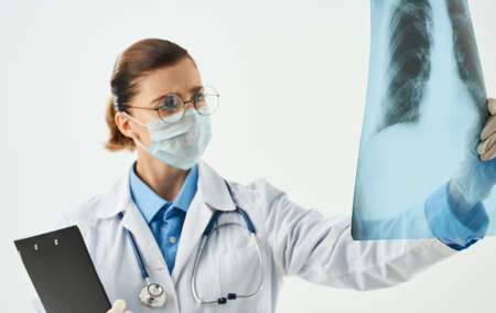 A woman doctor in a medical mask examines an X-ray on a light backgroundの写真素材