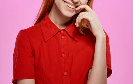 Charming woman in a red dress on a pink background gestures with her handsの写真素材