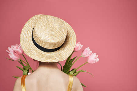 woman with hat back view bouquet of flowers as a gift pink backgroundの写真素材
