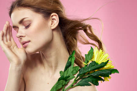 Beautiful woman naked shoulders yellow flower charm cosmetics pink backgroundの写真素材