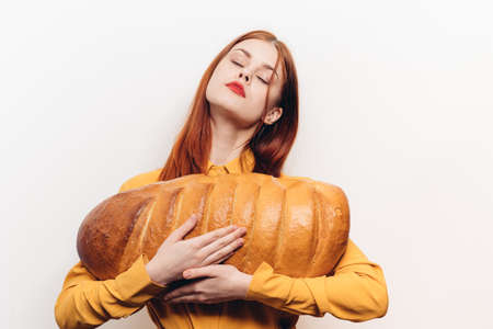 beautiful woman holding a loaf in her hands and bright makeup yellow shirt light backgroundの写真素材