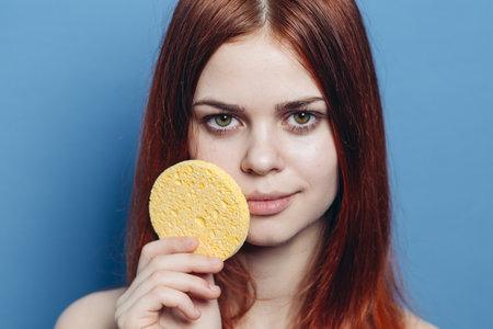 cute redhead woman shoulders wipes face with sponge skin careの写真素材