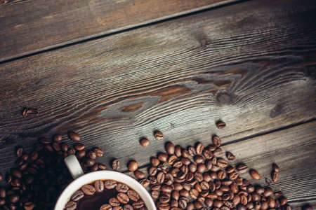 coffee beans scattered on a wooden table and a cup with a hot drink aromaの写真素材