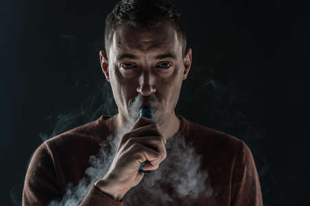 a man smokes a vape on a black background white smoke steam portrait close-up