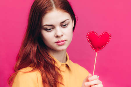 happy woman with red heart on stick on pink background and yellow shirtの写真素材