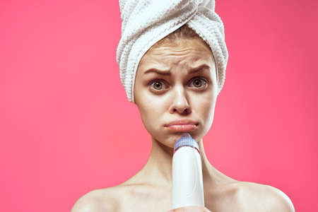 cheerful national woman with a towel on her head massagers in hands skin care spa treatments pink backgroundの写真素材