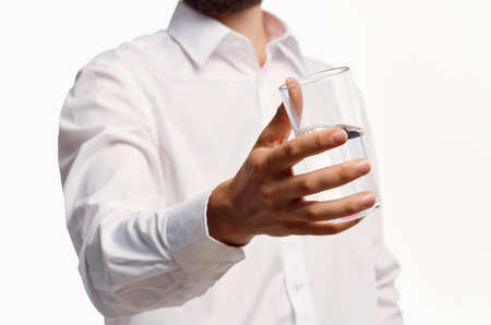 A gentleman in a white shirt holds a glass of water in his hand on a light backgroundの写真素材