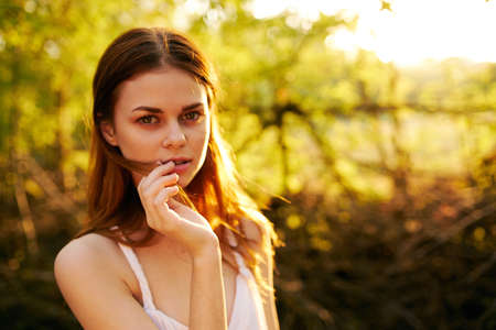 romantic woman in white dress gesturing with hands on nature in park