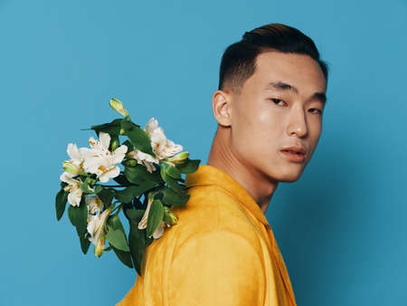 A man with a bouquet of flowers behind his back on a blue background and a yellow coatの写真素材