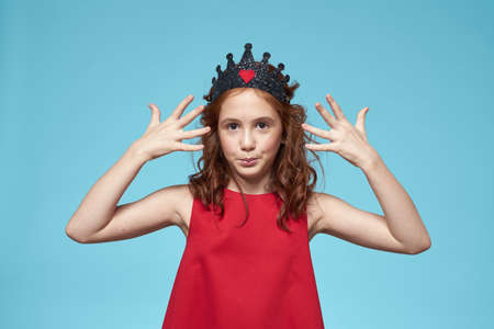 Girl with curly hair with a crown on her head red dress lifestyle blue background