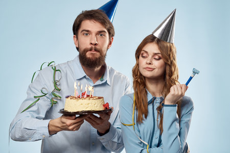 Birthday man woman in party hats on a blue background and cake with candlesの写真素材