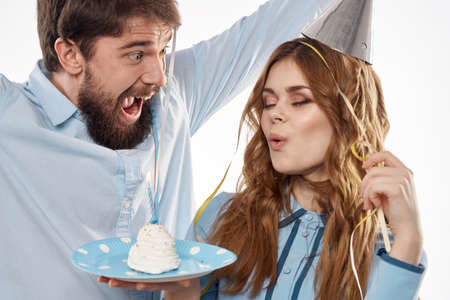 energetic man and woman with a cake and in hats celebrate a birthday on a light backgroundの写真素材