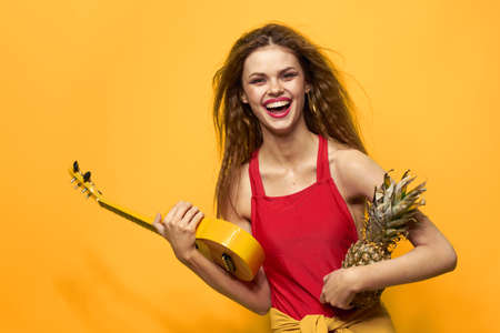 Cheerful woman in red ukulele t-shirt Exotic fruit yellow background lifestyleの写真素材