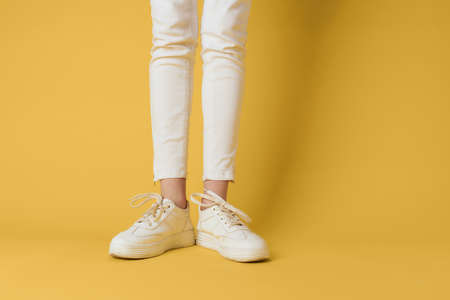 Female feet white sneakers attractive look fashion yellow backgroundの写真素材