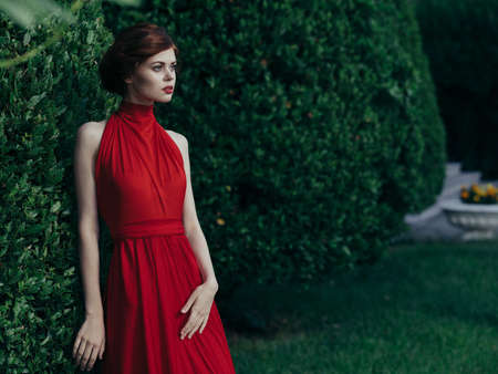 Pretty woman outdoors red dress luxury green bush walk Masqueradeの写真素材