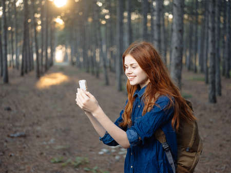 A woman travels in a pine forest with a mobile phone in her handの写真素材