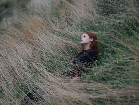 A woman in a black dress lies on dry grass in a meadow in the mountainsの写真素材