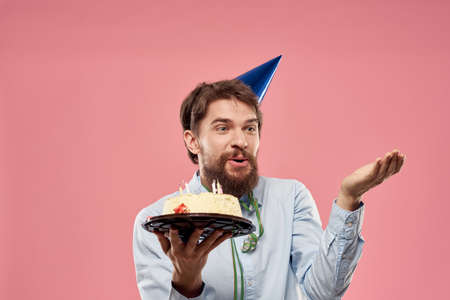 Bearded man with cake tongue on a pink background cropped view and a blue cap on his head