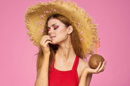 Woman with coconut cocktail in straw hat exotic vacation summer pink backgroundの写真素材