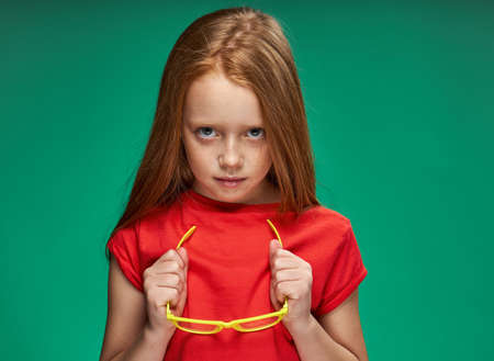 cute girl red hair gestures with hands emotions childhood school Green backgroundの写真素材
