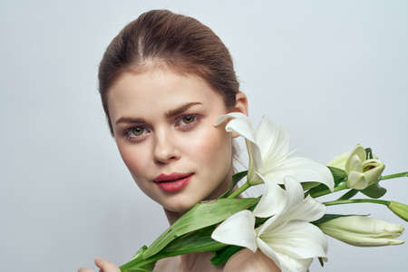 Beautiful girl with a bouquet of white flowers on a light background naked shoulders clean skin springの写真素材