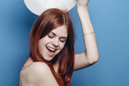 cheerful red-haired woman naked shoulders hat blue backgroundの写真素材
