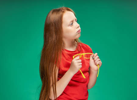 girl with red hair holding yellow glasses in her hands green background studio red t-shirt