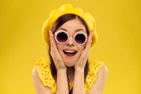 Happy woman in a yellow hat and fashionable glasses holds her hands near her face on a yellow background cropped view of emotions funの写真素材