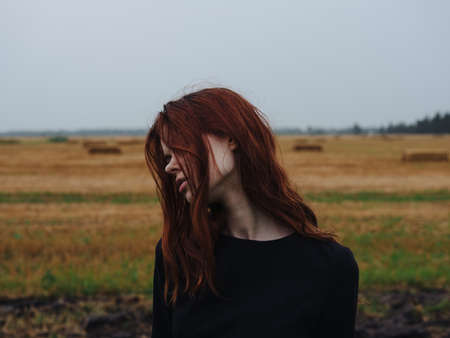 Portrait of a red-haired woman in a black dress in a field in nature cropped viewの写真素材