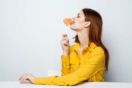 pretty woman with lollipop like in a yellow shirt sits at the table emotionsの写真素材