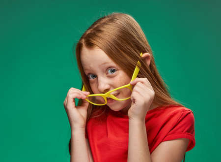 cheerful red-haired girl yellow glasses emotions green background childhoodの写真素材