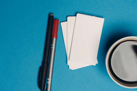 business cards on blue background and pen coffee cup top view