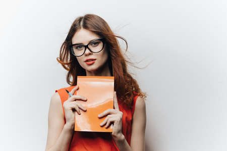woman in an orange sundress with a notebook in hand on a light background female student education...