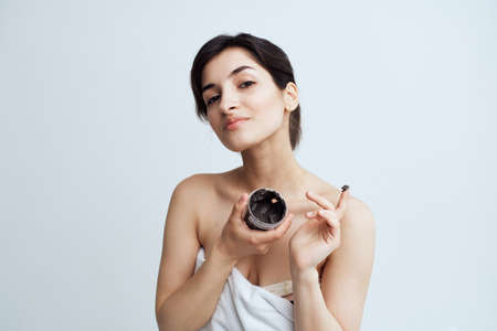 Pretty woman in white towel naked shoulders black cream in hands skin care spa procedureの写真素材