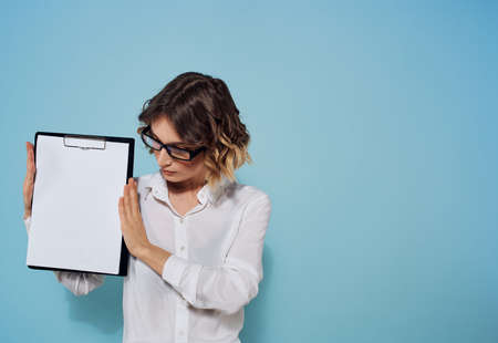 Business woman with a folder and a white sheet of paper on a blue background glasses on her faceの写真素材