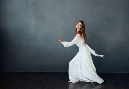 Charming lady in a white dress on a gray background dance gesticulating with her hands modelの写真素材