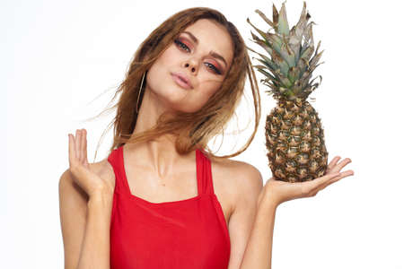 Woman with pineapple in hands wavy hair red t-shirt fruits summer vacation light backgroundの写真素材