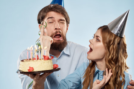 Birthday man woman in party hats on a blue background and cake with candlesの写真素材
