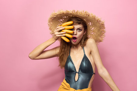 Woman in beach straw hat bananas holding fruits Exotic swimsuit pink backgroundの写真素材