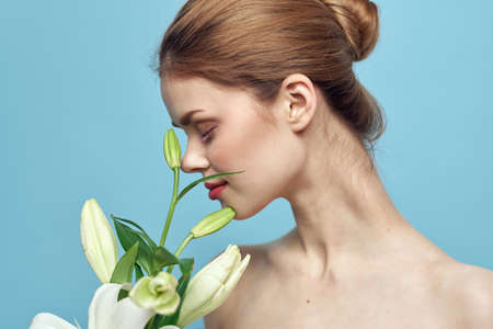 Beautiful girl with a bouquet of white flowers on a blue background cropped view naked shoulders portraitの写真素材